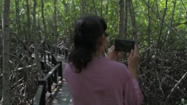 Tatil konsepti 4k Çözünürlük. Mangrov ormanında doğanın fotoğraflarını çeken Asyalı yaşlı bir kadın..