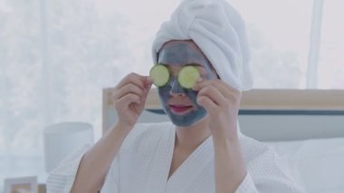 Spa konsepti 4k Çözünürlük. Asyalı kız yatak odasında gözlerine salatalık sürüyor..