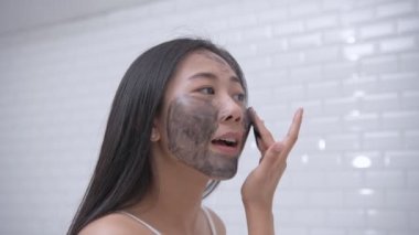 4k Çözünürlük 'ün güzellik konsepti. Genç bir Asyalı kadın yüzüne çamur sürüyor..