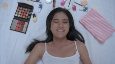 4k Çözünürlük 'ün güzellik konsepti. Asyalı kız, yatak odasındaki kozmetik ürünlerine gülerek gülümsüyor..