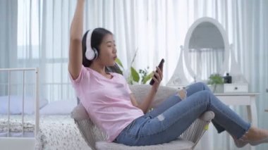 Tatil konsepti 4k Çözünürlük. Asyalı kızlar yatak odasında sandalyede oturmuş müzik dinliyorlar..