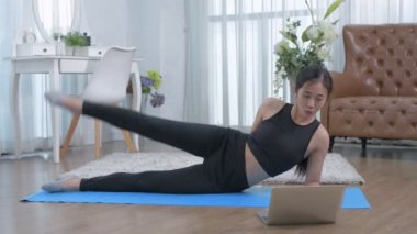 4k Çözünürlük alıştırması. Spor yapan genç bir kadın egzersiz yapıyor. Bacağını kaldırıyor. Halıda yatıyor..