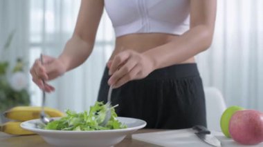 Sağlık konsepti 4k Çözünürlük. Spor sutyenli genç bir kadın evde salata yapıyor..