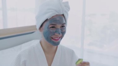 Spa konsepti 4k Çözünürlük. Asyalı kız yatak odasında gözlerine salatalık sürüyor..