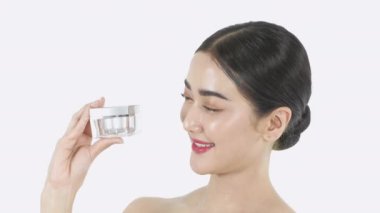 4k Çözünürlük 'ün güzellik konsepti. Beyaz arka planda krema şişeleri sunan genç bir kadın..