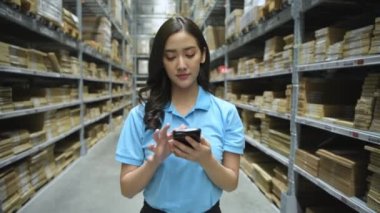 4k Kararlılığın iş konsepti. Asyalı bir kadın bir depoda cep telefonundan yapılan başvuru ile ürünleri kontrol ediyor..