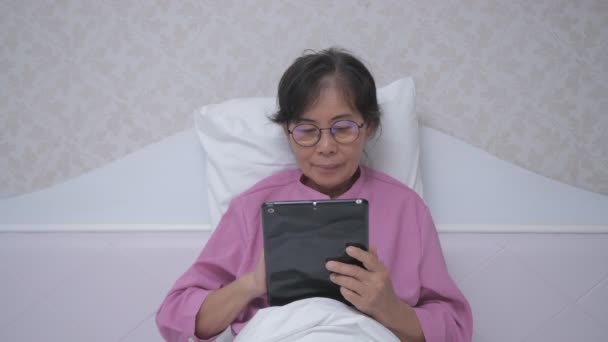 假日4K解像度的概念 一位亚洲老妇人对科技感兴趣 在卧室里用平板电脑 — 图库视频影像