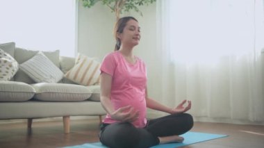 Hamile kadın konsepti 4k Kararlılık. Sağlıklı kalmak için evde yoga yapan genç bir kadın..