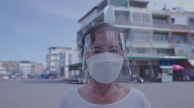 Sağlıklı bir 4k çözünürlük kavramı. Yaşlı bir kadın gülümsüyor ve şehrin arka planında bir maske takıyor..