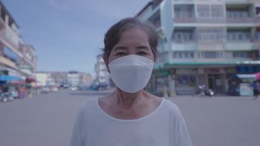 Sağlıklı bir 4k çözünürlük kavramı. Yaşlı bir kadın gülümsüyor ve şehrin arka planında bir maske takıyor..