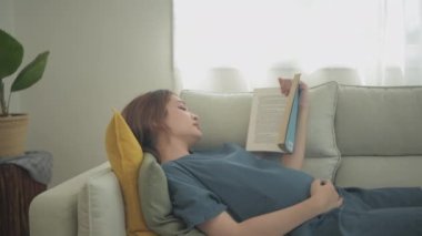 Hamile kadın konsepti 4k Kararlılık. Oturma odasında kitap okuyan bir kadın..