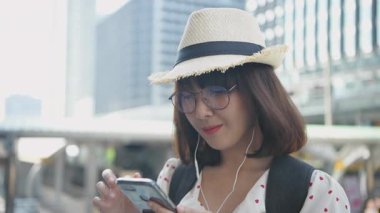 Seyahat konsepti 4k Çözünürlük. Şehirde cep telefonuyla müzik dinleyen Asyalı bir kadın..
