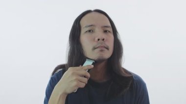Sağlık konsepti 4k Çözünürlük. Genç bir Asyalı beyaz arka planda elektrikli makasla tıraş oluyor..