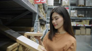 4k Kararlılığın alışveriş kavramları. Asyalı bir kadın bir ürün kutusunu alıyor ve satın almadan önce bir mobilya mağazasının deposunda inceliyor..