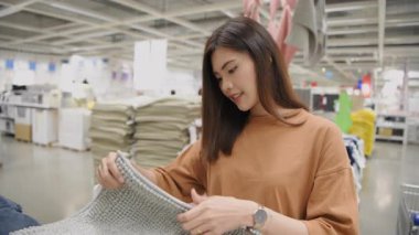4k Kararlılığın alışveriş kavramları. Asyalı bir kadın bir mağazada paspası inceliyor, seçmeden önce dokusunu hissediyor..