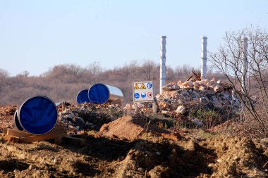 Büyük çaplı boruları birleştirmek için küçük tepenin üzerine bırakılan petrol boru hattı şantiyesi ve soğuk kış gününde ağaçlar ve kayalarla çevrili arka planda üç uzun sanayi bacası.