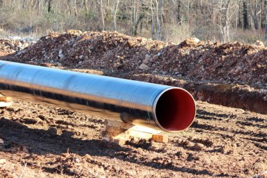 Yerli petrol boru hattı şantiyesindeki parlak yeni geniş çaplı boru, soğuk kış günlerinde kayalar ve kuru bitki örtüsüyle çevrili ıslak toprağın üzerindeki ahşap desteklerle destekleniyor.
