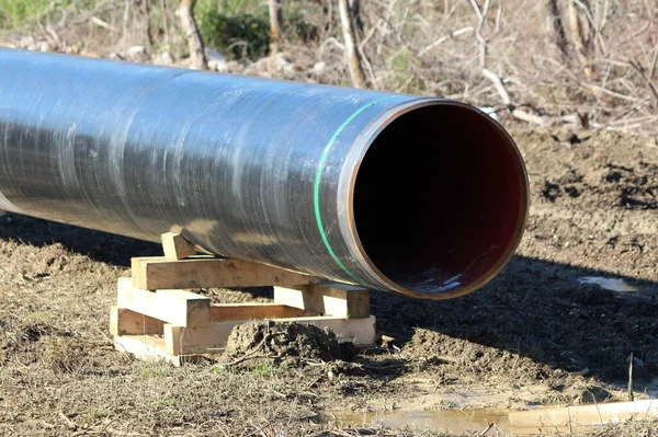 Soğuk kış gününde kuru bitki örtüsü ve çimlerle çevrili ıslak toprağın üzerindeki ahşap desteklerle desteklenen yerel petrol boru hattı şantiyesindeki büyük çaplı boru.