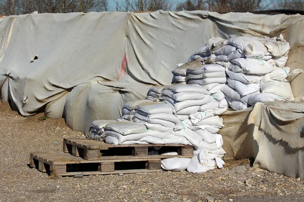 Sele karşı korunmak için kullanılan yeni ve eski kısmen kırılmış kum torbaları merdiven şeklinde ahşap paletlere yerleştirildi. Kalın beyaz jeotektil kumaşlarla kaplı kutu bariyerlerinden oluşan geçici sel koruma duvarının yanına.