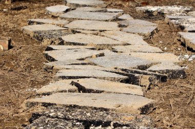 Yıkılmış asfalt yolların kırık çatlak levhaları soğuk kış gününde kuru çimlerle karışık ıslak toprağın üzerinde bir yol oluşturmak için bir araya toplanmış.