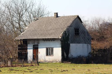 Kırık kiremitleri ve kırık camları olan, arka planda yaprakları olmayan, çimensiz, güneşli kış günlerinde ağaçlarla çevrili terk edilmiş, eski ahşap bir aile evi.