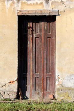 Kırık açık sarı banliyö aile evinin duvarına monte edilmiş paslı metal çerçeveli eski ahşap giriş kapıları ve sıcak kış gününde önünde işlenmemiş çimenler.