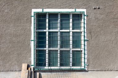 Beyaz ahşap çerçeveli antika eski pencere ve metal parmaklıklar, sanayi duvarına tahta tahtalar ve ön taraftaki tel örgülerle örülmüş.