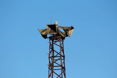 Dört büyük sivil savunma sirenleri açık mavi arka planda, paslı metal yapının üzerine monte edildi.