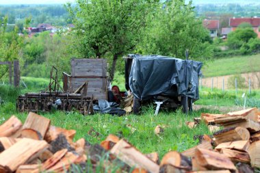 Eski, harap olmuş ahşap traktör römorkları. Dört tekerleği kalın naylonla kaplı. Etrafı çeşitli paslanmış tarım ekipmanlarıyla çevrili.