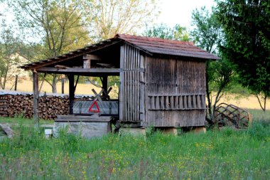 Dar dikey tahtadan yapılmış mısır koçanları kurutmak ve depolamak için kullanılan eski ve eski bir antika ahşap ahşap ahşap ahşap kulübe. Çatı kiremitleriyle kaplı açık depolama alanı kesilmemiş çimenlerle karıştırılmış tarımsal ekipmanlarla kaplı.