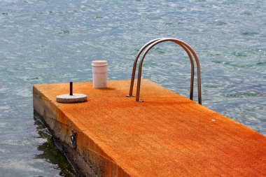 Turuncu renkli harap olmuş beton iskele üzerinde çeşitli metallerle kaplanmış. Bir tarafında paslanmaz çelik merdivenler var. Soğuk bahar günü paslanmaz denizle çevrili.