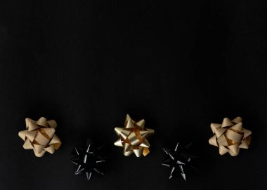 Altın fiyonklar ve kurdeleler siyah arka planda yatar. Hediyeleri paketliyorum. Paketleme