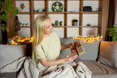 Sarışın bir kız kanepeye oturmuş sevgililer günü için hediye paketliyor.