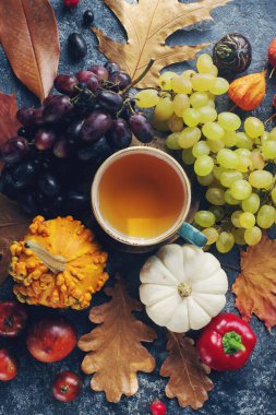 Sıcak sonbahar kompozisyonu, bir fincan çay, balkabağı, üzüm, koyu taş masadaki sonbahar yaprakları, Cadılar Bayramı veya Şükran Günü için mevsimlik dekorasyon, 