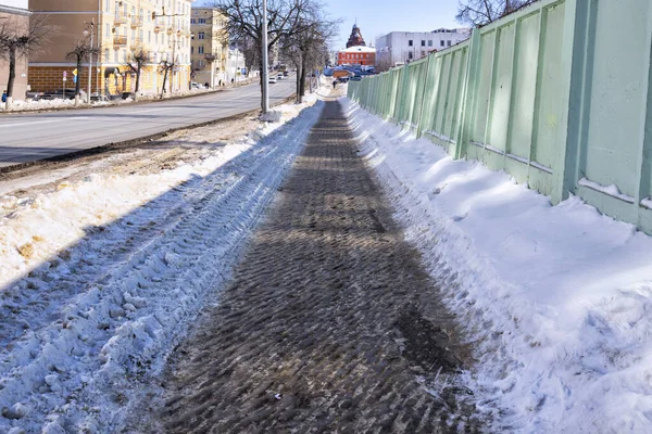 The pedestrian sidewalk is covered with ice. learing the roadway from snow and ice