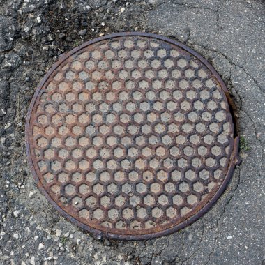 Asfalt manzaralı eski metal rögar kapağı. Bal peteği deseni.