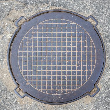 Eski metal paslı rögar kapağı şehrin asfalt manzaralı kanalizasyon kapağını kapatıyor. Kafes deseni