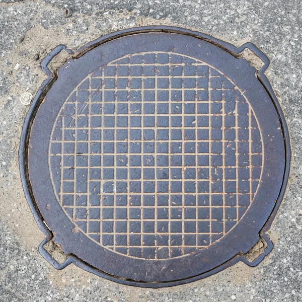Eski metal paslı rögar kapağı şehrin asfalt manzaralı kanalizasyon kapağını kapatıyor. Kafes deseni