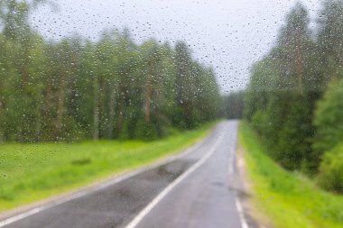 Yaz kırsalında yağmur damlalarıyla iki şeritli yol manzarası.