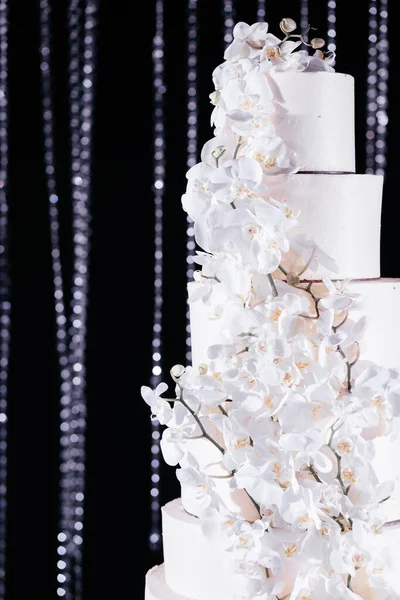 Cerrar pastel de boda decorado con orquídeas blancas. Pastel de boda en el fondo oscuro brillante — Foto de Stock