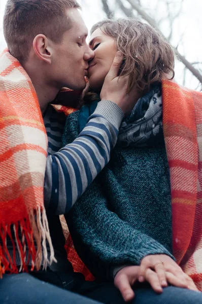 Χριστούγεννα, εποχή και άνθρωποι έννοια - ευτυχισμένο ζευγάρι κάθεται καλύπτονται με μια κουβέρτα και φιλιά κρατώντας ο ένας τον άλλο χέρι σε εξωτερικούς χώρους το χειμώνα πάρκο — Φωτογραφία Αρχείου
