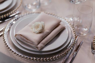 Üstünde bej peçete olan tabaklar. Lokantada lüks masa hazır. Bardaklar ve tabaklar. Dekorasyon. Bej arka plan. Düğün ziyafeti. 