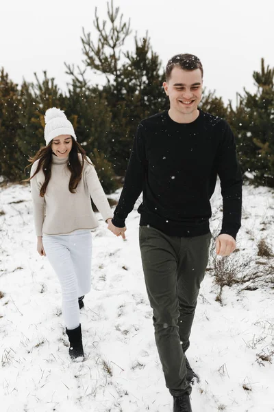 Νεαρός άντρας και γυναίκα να πηγαίνουν στο χιόνι στο πευκοδάσος κρατώντας ο ένας το χέρι του άλλου. Αγάπη, σχέση, χειμερινές διακοπές. Χειμερινό ζευγάρι ιδέες φωτογραφία — Φωτογραφία Αρχείου