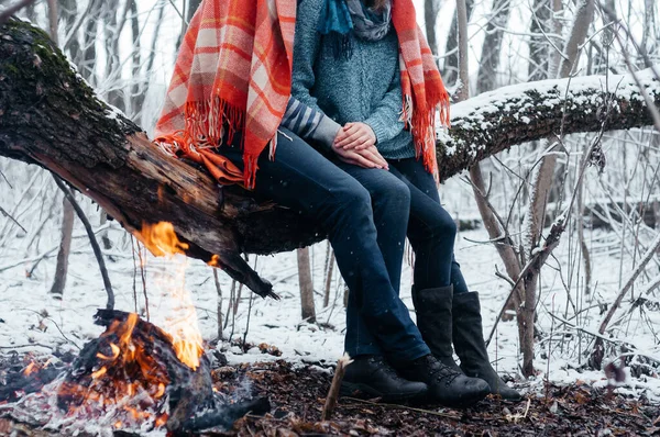 Ανέκφραστο ζευγάρι ερωτευμένο να κάθεται μαζί στο ξύλινο κλαδί κοντά στο τζάκι στο χειμερινό δάσος. Εραστές για πικνίκ το χειμώνα — Φωτογραφία Αρχείου