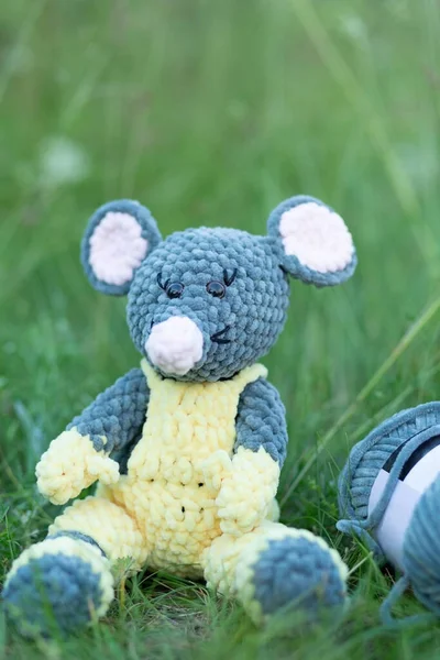 Handmade knitted toy. Knitted mouse in yellow overalls on the grass with place for your text. High quality photo