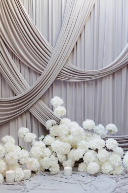 Beyaz çiçekler yumuşak, örtülü kumaşa karşı narin bir şekilde dinleniyor ve özel bir olay için sakin bir ortam yaratıyor. Ortam huzurlu ve davetkar..