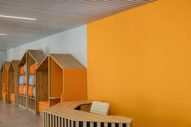 Parlak ve neşeli bir resepsiyon alanında turuncu duvarlar ve ahşap mobilyalar yer alıyor..