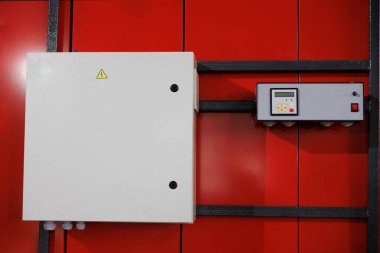 Bir kontrol paneli, birden fazla bağlantı noktası ve güvenli işlemler için uyarı işaretleri olan canlı kırmızı bir duvara sıkıca bağlanır..