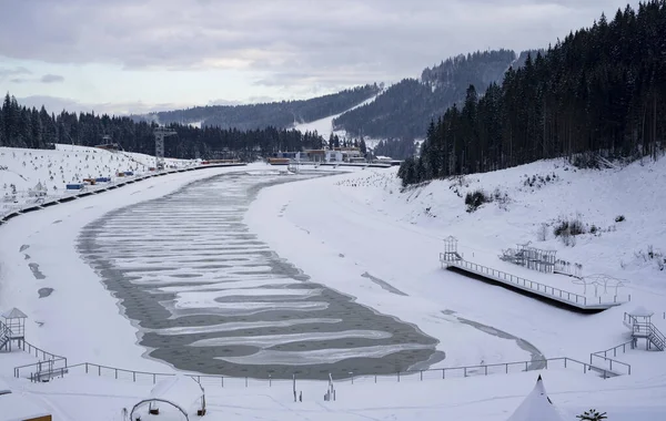 An artificial lake in the mountains with good infrastructure for recreation, covered with snow and ice. The lake is used for artificial snowmaking of the ski resort