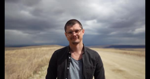 Portrait of a smiling guy with glasses outdoors in cloudy weather — Stock Video